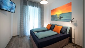 Un dormitorio con cama, cortinas, un cuadro, un televisor y una lámpara de pie.