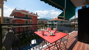 Un balcón con mesa y sillas rojas, un toldo verde y vistas a edificios y montañas.