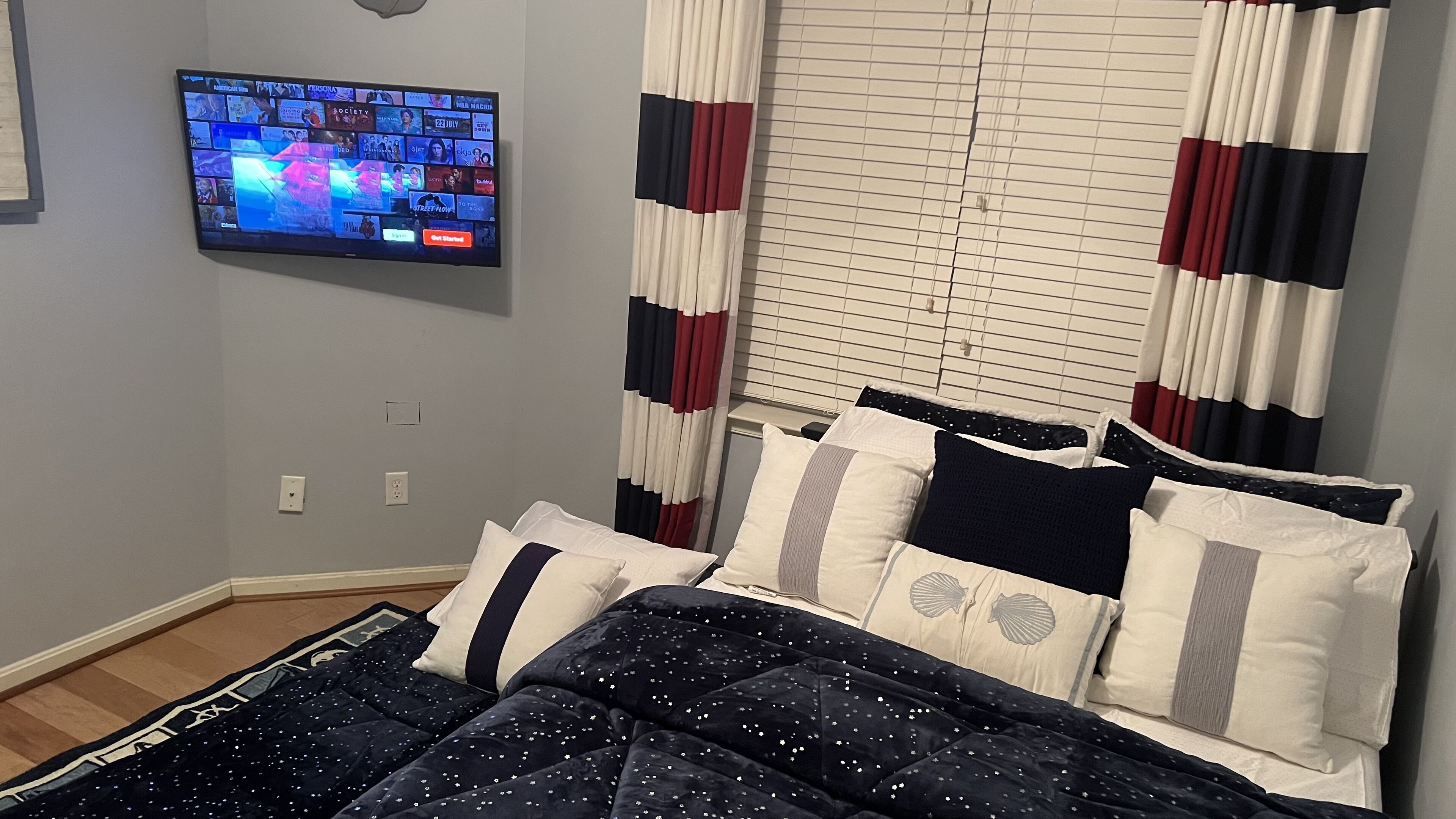 A bedroom with a bed, a television mounted on the wall, and a window with curtains.