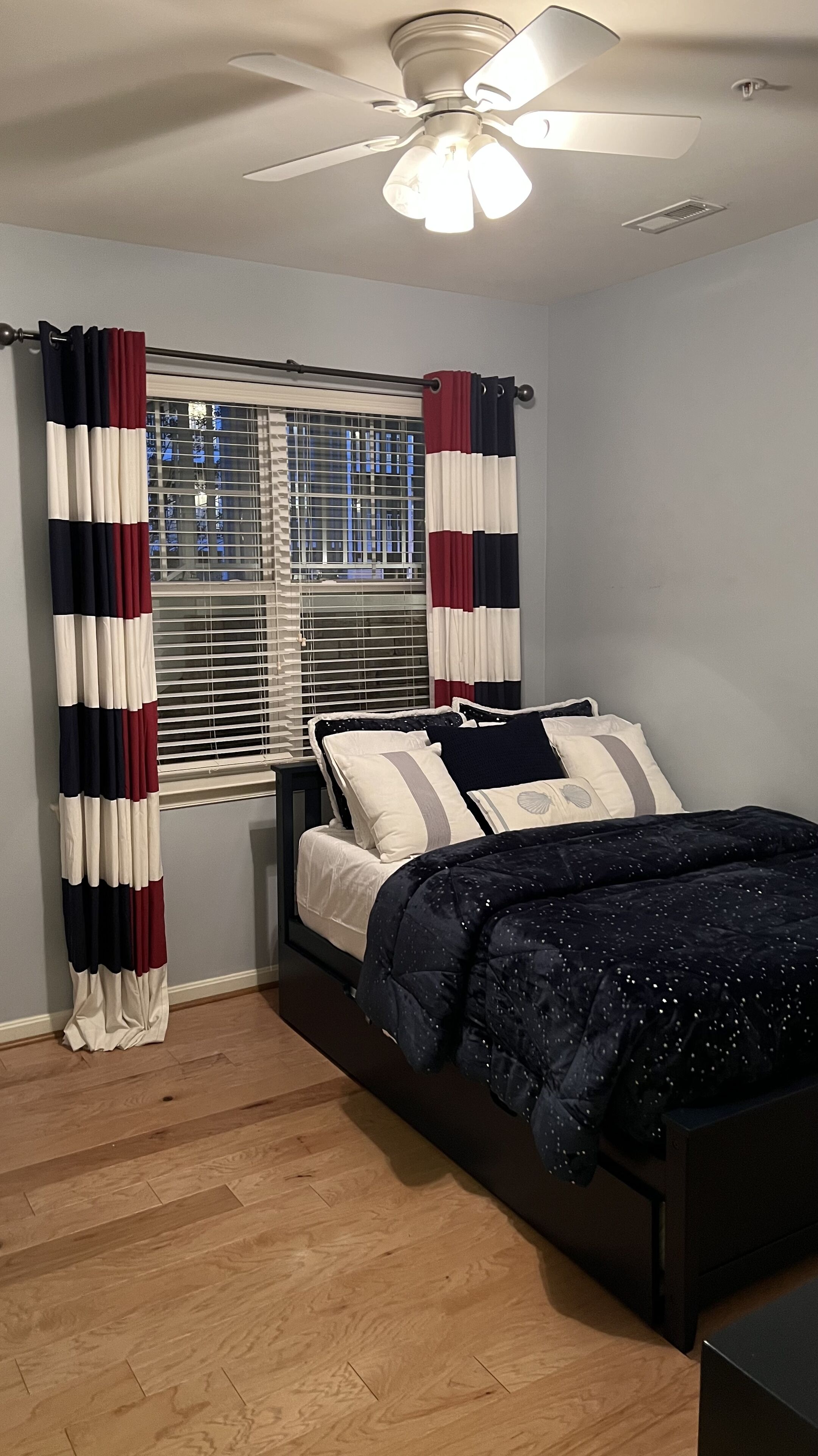 A bedroom with a bed, a ceiling fan, and a window with blinds.