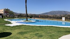 Une piscine avec un palmier, un espace clôturé et une vue sur les montagnes en arrière-plan.