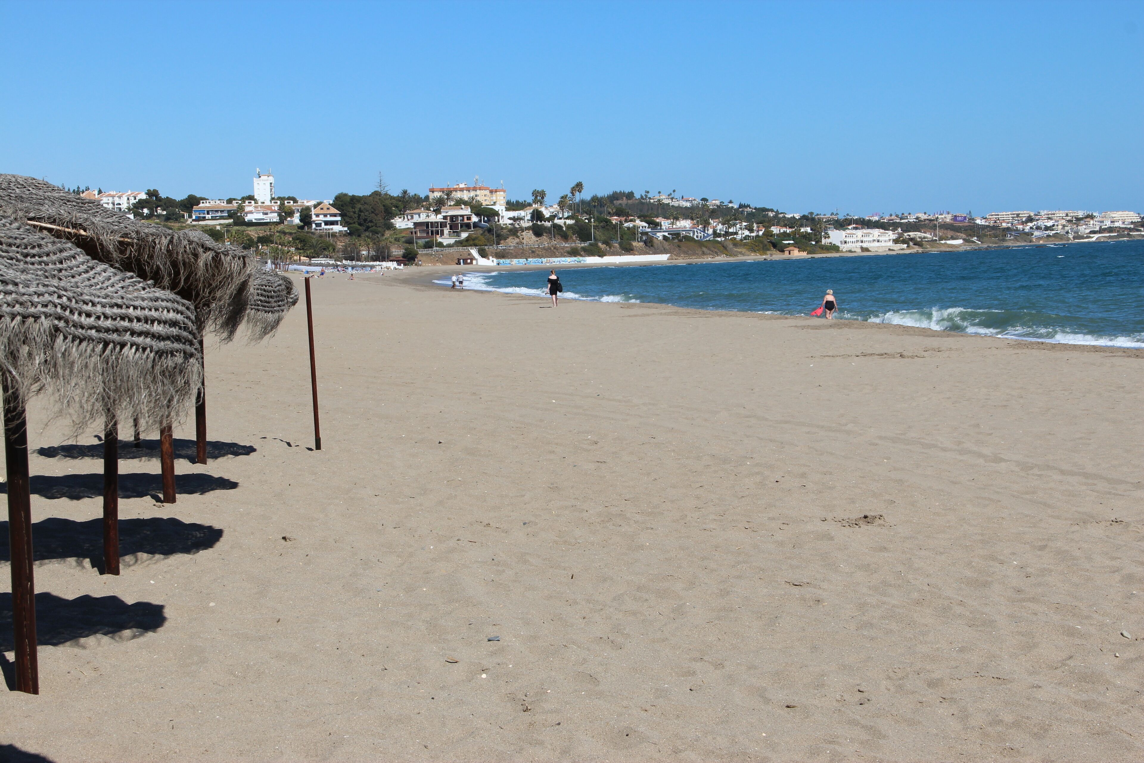 A beach with straw umbrellas and a clear view of the ocean.