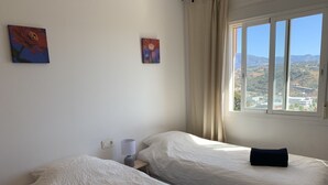 Une chambre avec deux lits, une fenêtre donnant sur un paysage et deux tableaux accrochés au mur.