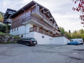 A multi-story building with balconies, a parking area, and a stone wall.