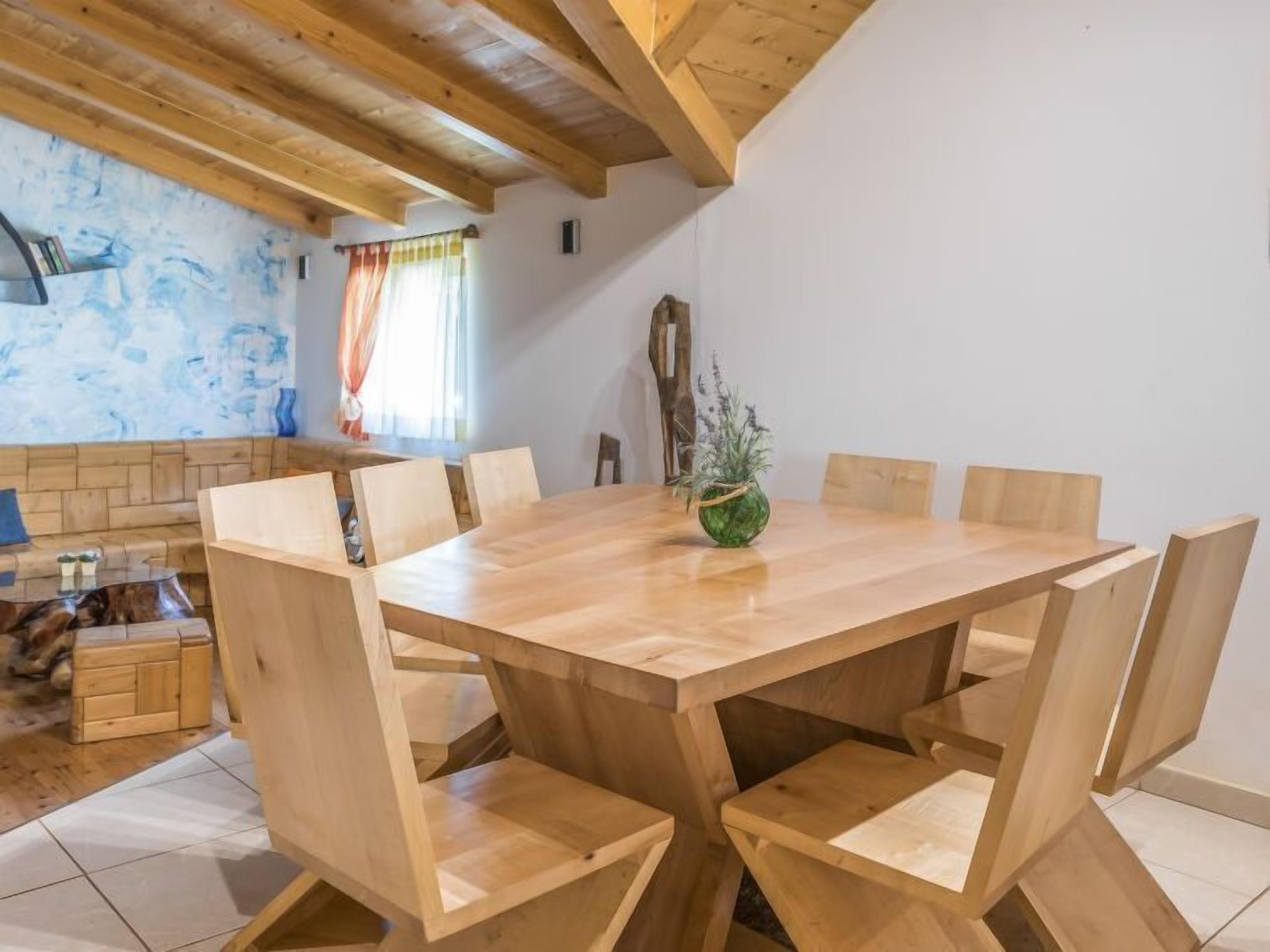 A wooden dining table with six chairs, a wooden bench, and a small plant on the table.