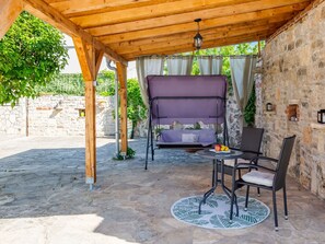 Relax in a serene outdoor seating area under a pergola, surrounded by lush greenery and a stone wall.