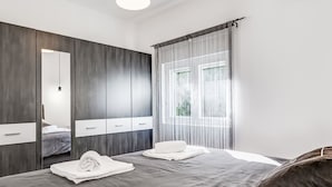 Un dormitorio moderno con una cama grande, un armario, un espejo y una ventana con cortinas translúcidas.