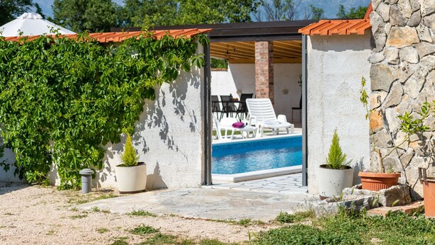 Zona de piscina con vista a montañas, un porche cubierto y un muro de piedra.