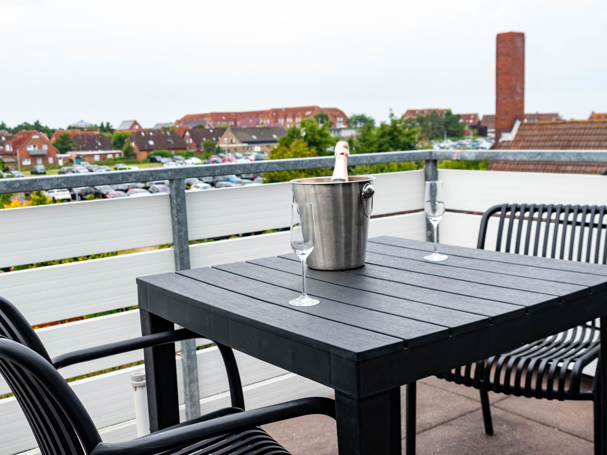 A terrace with a table and chairs, a champagne bottle, and a view of a parking lot and buildings.