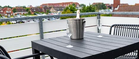 Eine Terrasse mit Tisch und Stühlen, einer Champagnerflasche und Blick auf einen Parkplatz sowie Gebäude.