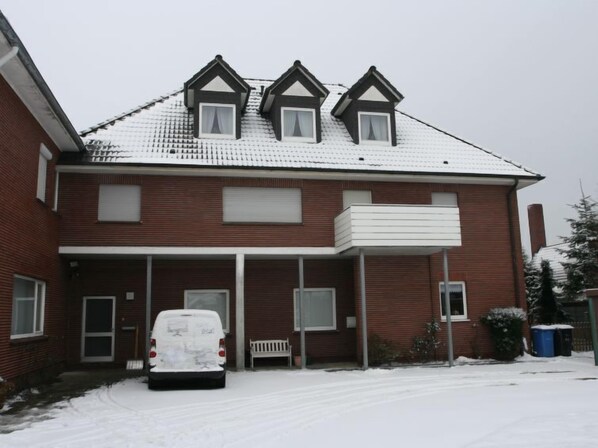 Une maison à deux étages, construite en briques, avec un porche abrité, une voiture garée devant et de la neige sur le toit.