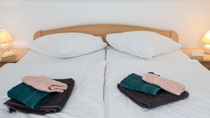 Een net opgemaakt bed met witte lakens, twee kussens en een stapje gevouwen handdoeken in verschillende kleuren.