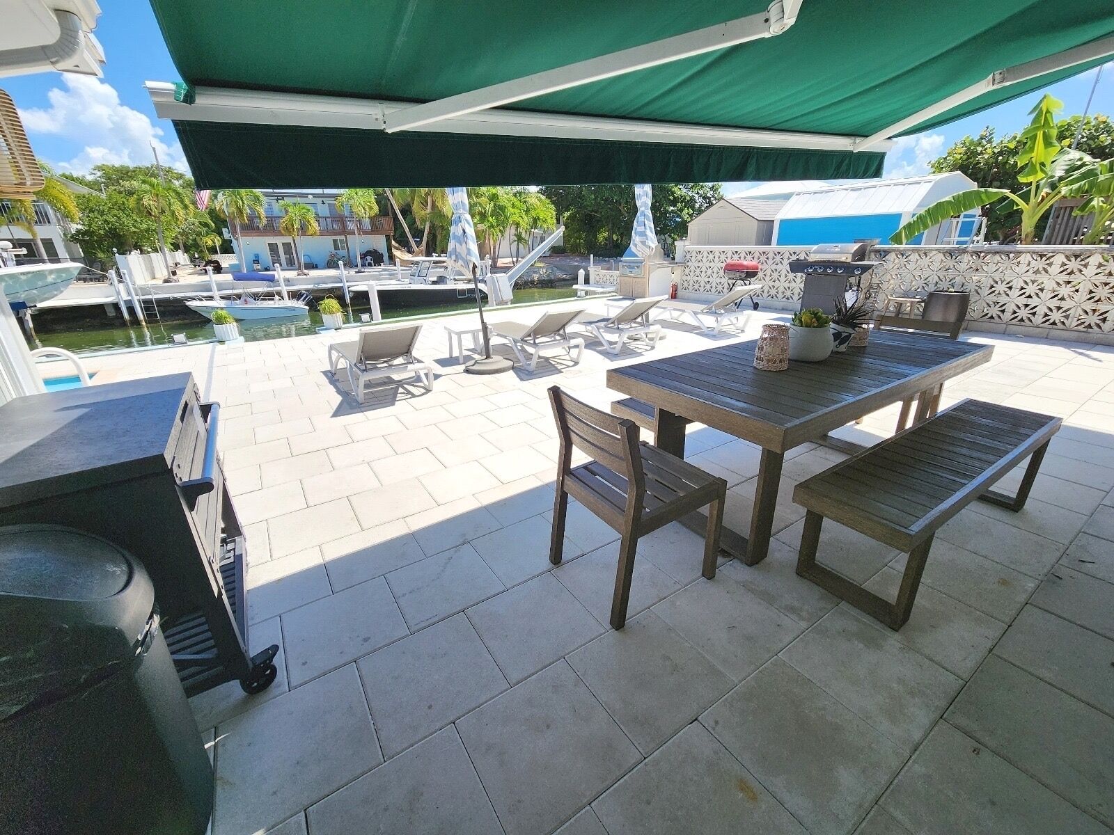 A patio area with a grill, outdoor seating, and a view of a pool and boats.