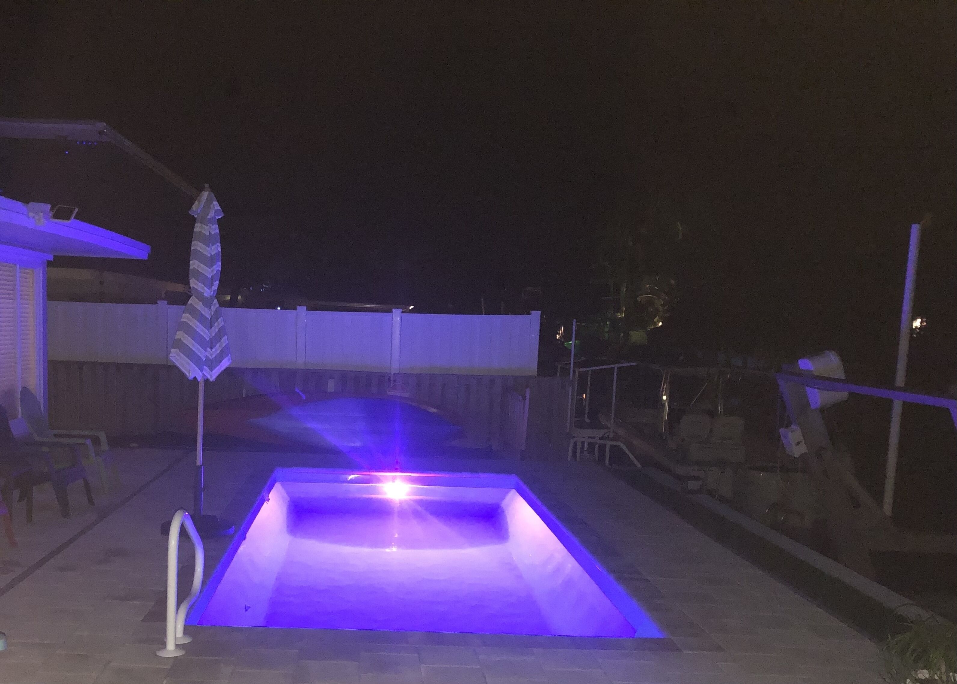 A rectangular swimming pool with a blue light at night.