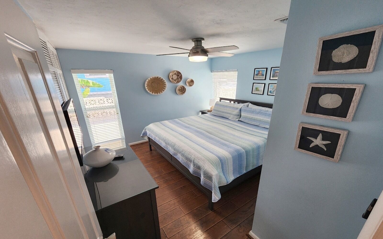Un dormitorio con cama, ventilador de techo y adornos en la pared, incluyendo cuadros enmarcados y cestas tejidas.