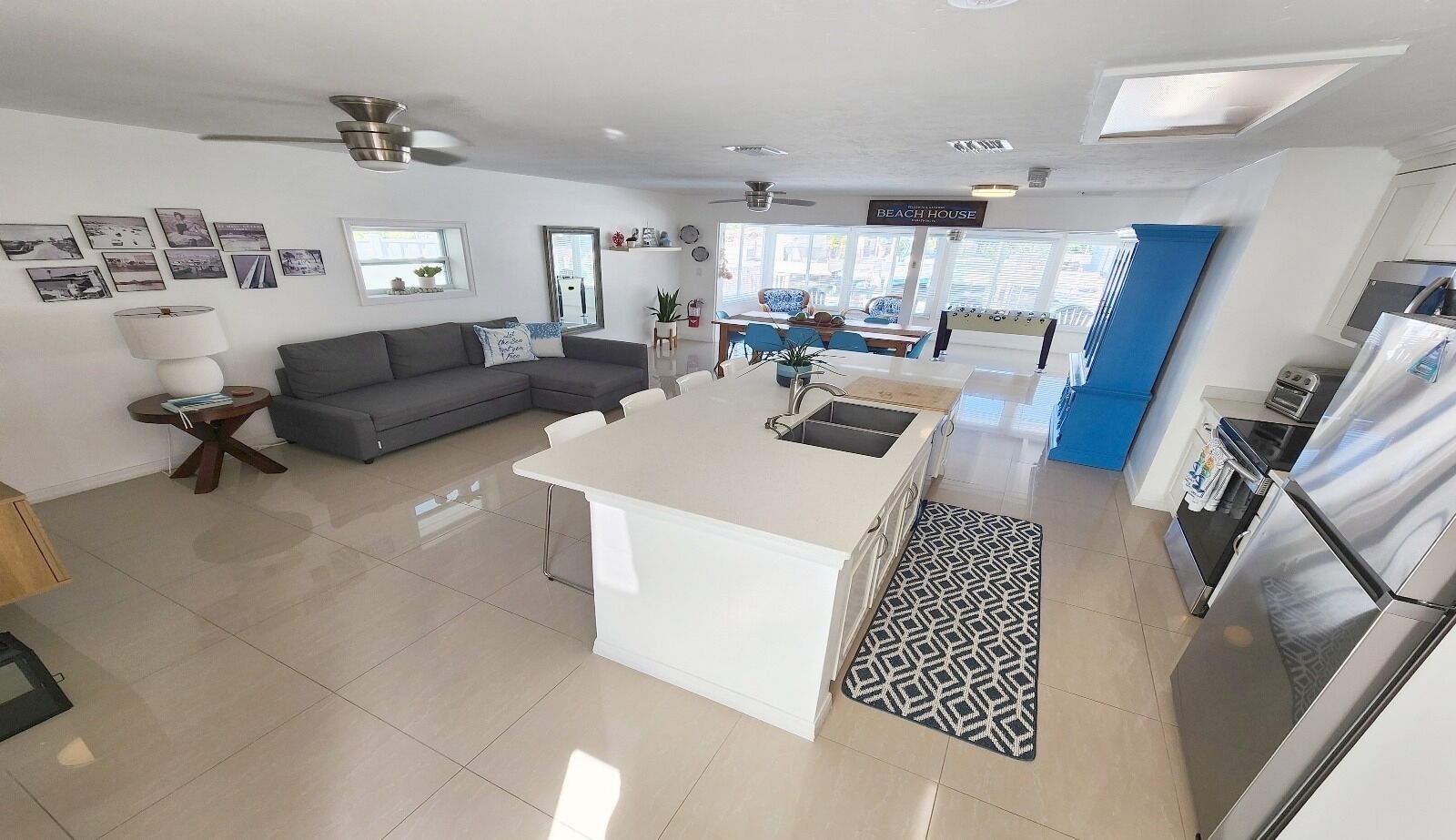 Een moderne keuken met een centraal eiland, een eethoek met blauwe stoelen en een grijze bank.