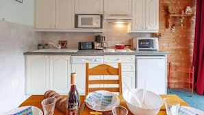 Une cuisine avec des meubles blancs, un four à micro-ondes, un grille-pain et une table à manger mise avec des assiettes, des verres et une bouteille.
