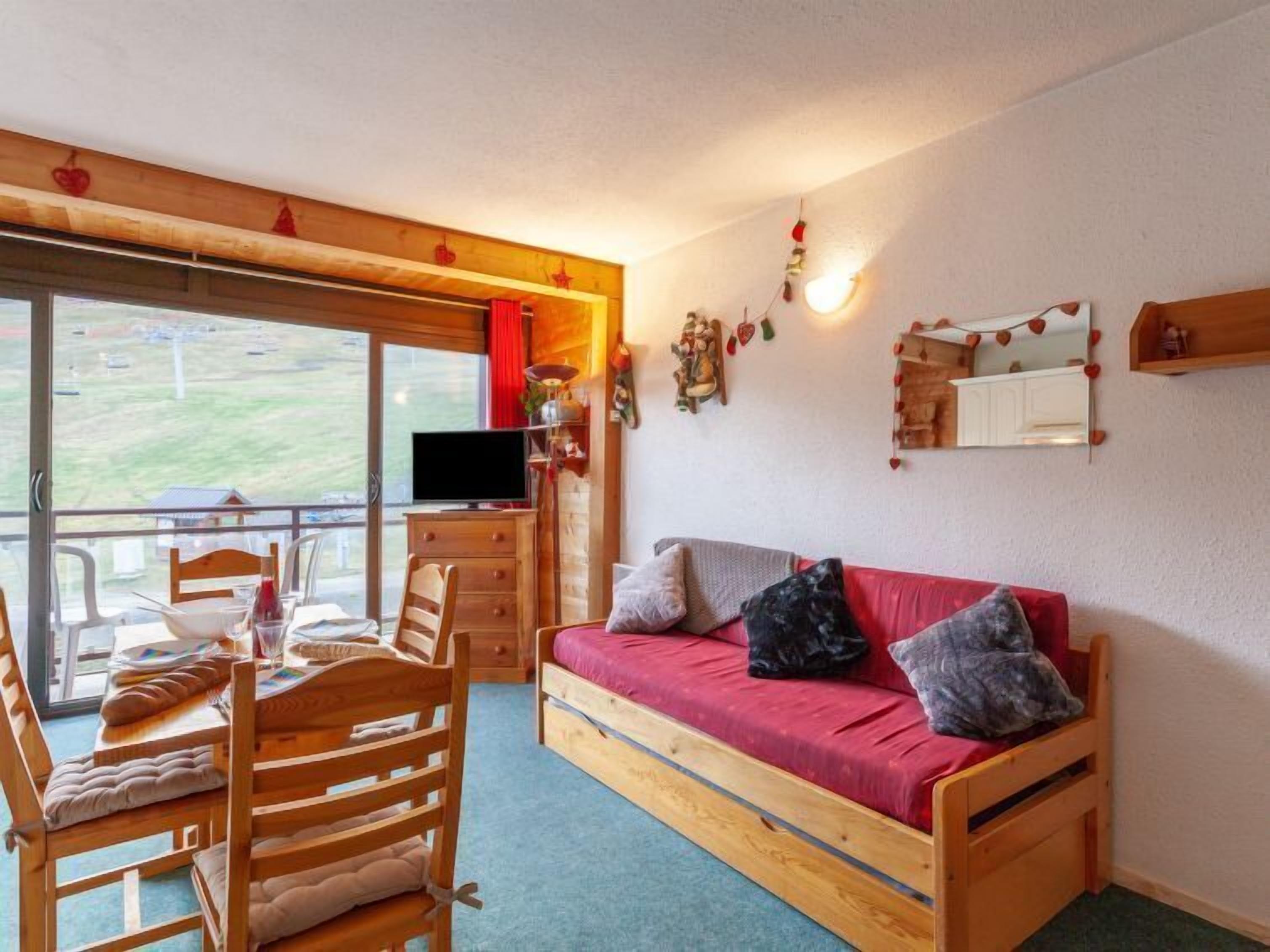 Una habitación acogedora con un sofá de madera, una mesa de comedor con sillas, un televisor y un balcón con vistas.