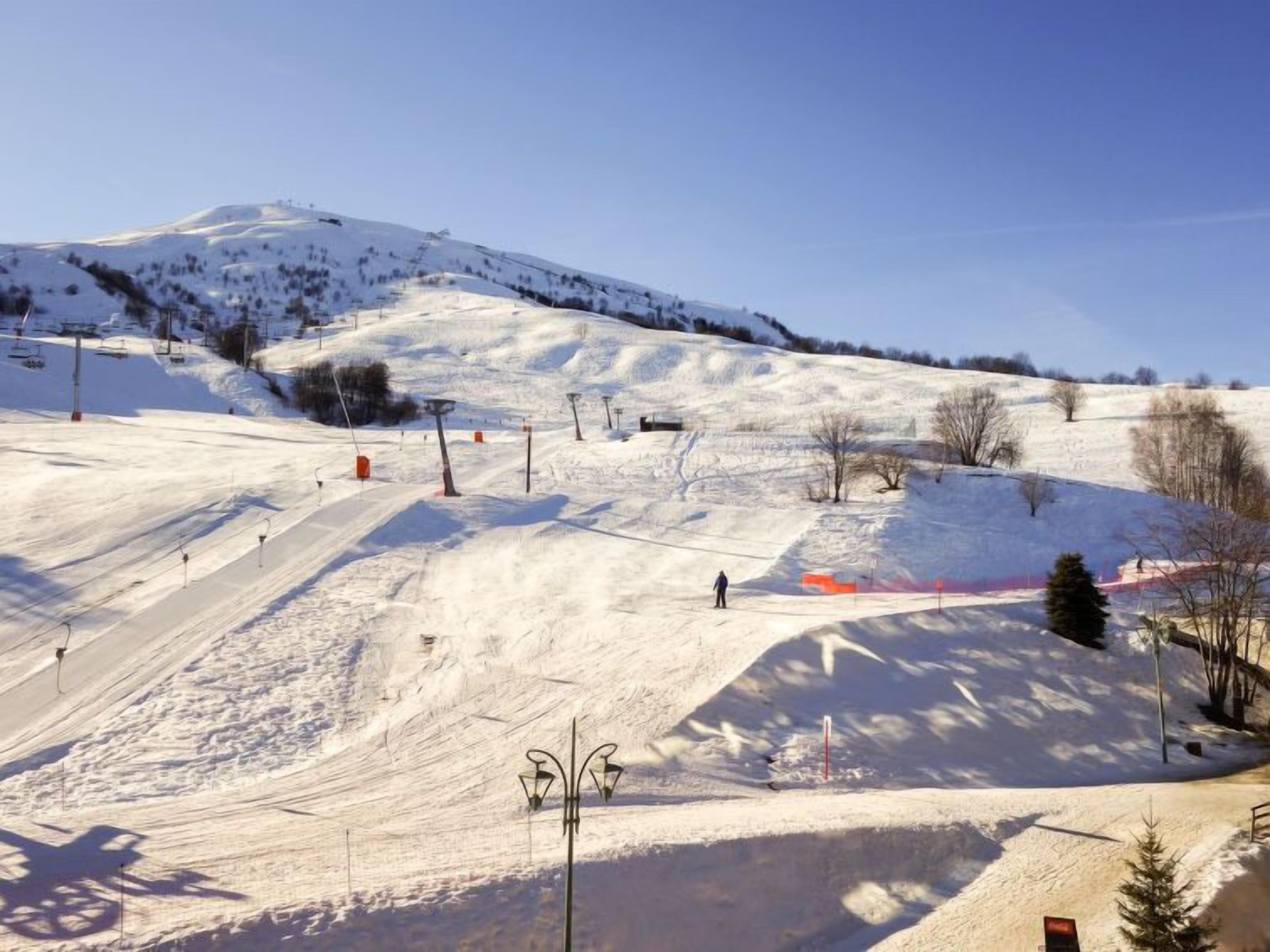 Une piste de ski enneigée, avec des remontées mécaniques, des arbres et un ciel dégagé.