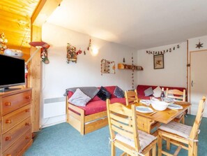 Een gezellige kamer met een houten bank, een eettafel met stoelen, een televisie op een houten kast en diverse wanddecoraties.