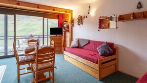 Une pièce confortable avec un lit en bois, une télévision, une table à manger avec des chaises et une grande fenêtre donnant sur l’extérieur.