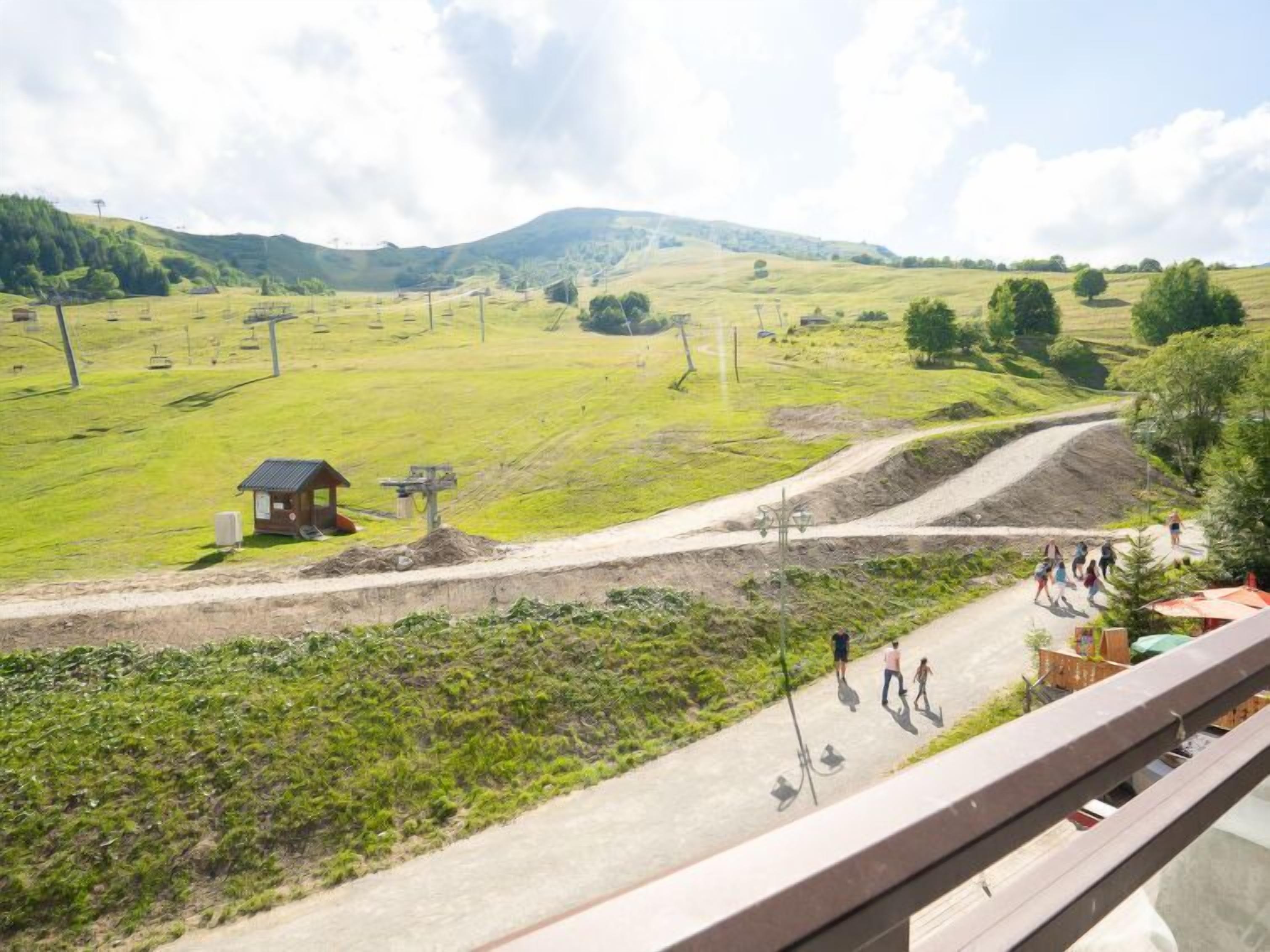 Een landelijk landschap met een onverharde weg, een klein houten gebouw en een groep mensen die lopen.