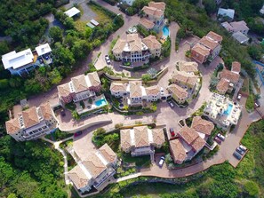 Vista aérea de uma área residencial com várias casas, cada uma com piscina e cercada por vegetação.