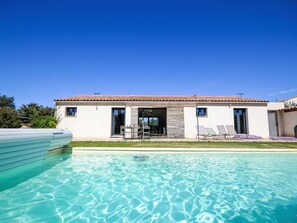 Ett modernt hus med en swimmingpool, en uteplats med solstolar och en klarblå himmel.