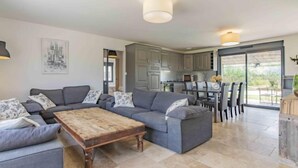 A modern living room with a grey sectional sofa, a wooden coffee table, and a dining area with a glass door leading to a patio. - L'Oliveraie by Interhome (Pernes les Fontaines)