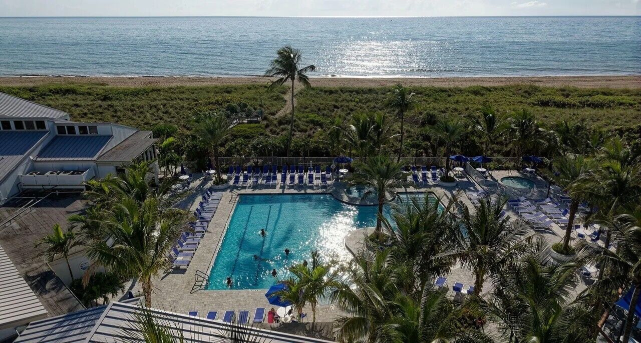 A pool area with lounge chairs, a swimming pool, and a view of the ocean.