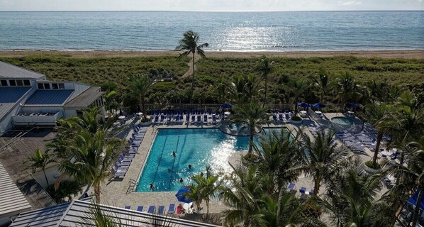 A pool area with lounge chairs, a swimming pool, and a view of the ocean.