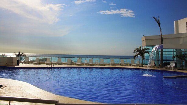 A pool with a view of the ocean, lounge chairs, and a building with a water feature. - Apartament w/ Sea View in Palmetto - Bocagrande Cartagena (Cartagena)