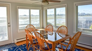 A dining area with a table and chairs, large windows, and a ceiling fan. - Three bedroom homes with wonderful views of Swan River and Nantucket Sound (Dennis Port)