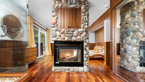 A modern interior with a stone fireplace, wooden cabinets, and a glass door. - Incredible Mid-Century Modern Waterfront Home on West Bay, on M22 - Sleeps 12 (Suttons Bay)