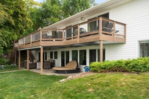 A two-story house with a covered patio area, a wooden deck, and a small outdoor seating area with a chair and a table.