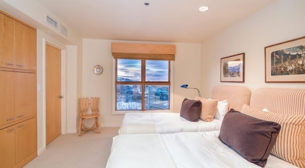 A bedroom with two beds, a window with a view, wooden furniture, and artwork on the walls. - Penthouse At The Peaks 746 (Mountain Village)