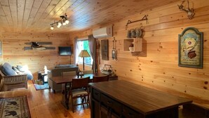 Interior acogedor de una cabaña con paredes de madera, una zona de comedor, un sofá y un televisor montado en la pared.