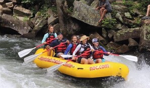 A group of people in a yellow raft with paddles, navigating a river surrounded by rocks and greenery. - Beautiful North Carolina Mountain View Cabin  near White water rafting NOC (Bryson City)