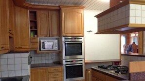 Een keuken met houten kastjes, een magnetron, een oven en een gasfornuis.