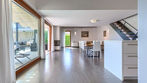 A spacious living area with a large sliding glass door leading to an outdoor patio, a dining area with a table and chairs, and a kitchen with white cabinets and a staircase.
