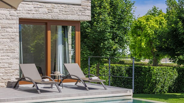 A poolside area with two lounge chairs and a small table, a stone wall, and a glass door.