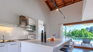 A modern kitchen with a central island, bar stools, a microwave, and a view of an outdoor pool area.