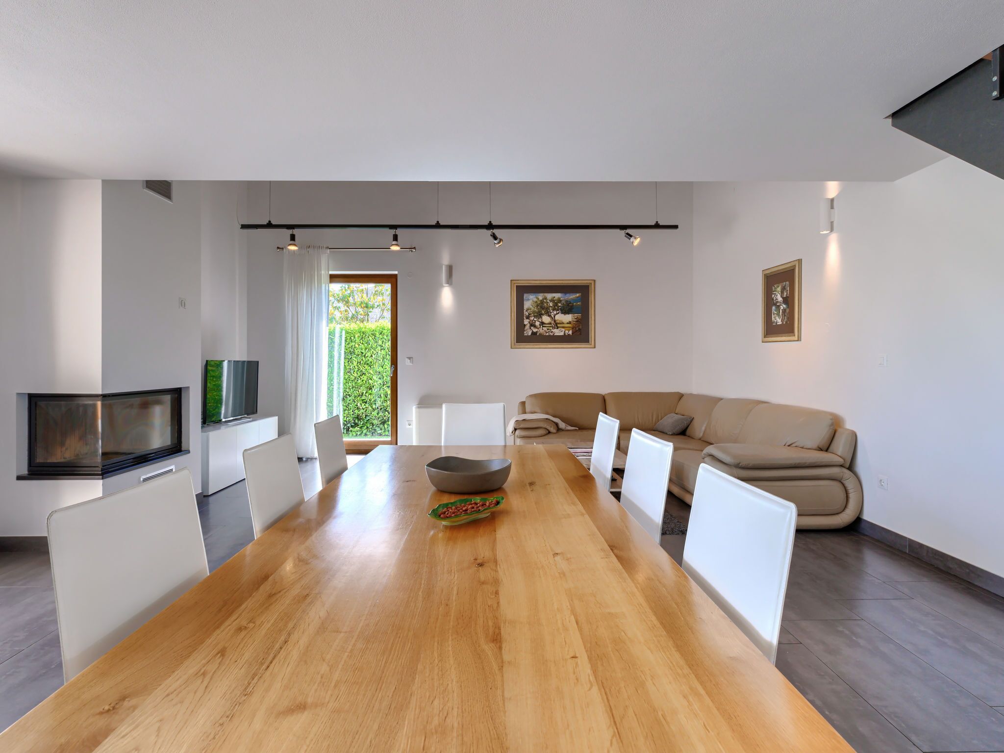 Een moderne woonkamer met een houten eettafel, witte stoelen, een beige bank en een flatscreen televisie.