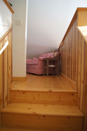 Una escalera de madera conduce a una habitación pequeña con una cama a cuadros y una mesita.