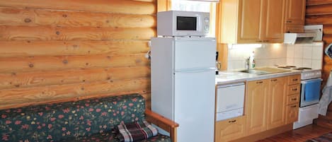 A compact kitchen with a refrigerator, microwave, and stove. There's a wooden bench with a floral cushion and a patterned rug.