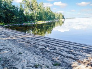 Hiekkainen ranta, jonka vieressä on tyyni järvi, ja rantaa ympäröi tiheä metsä.