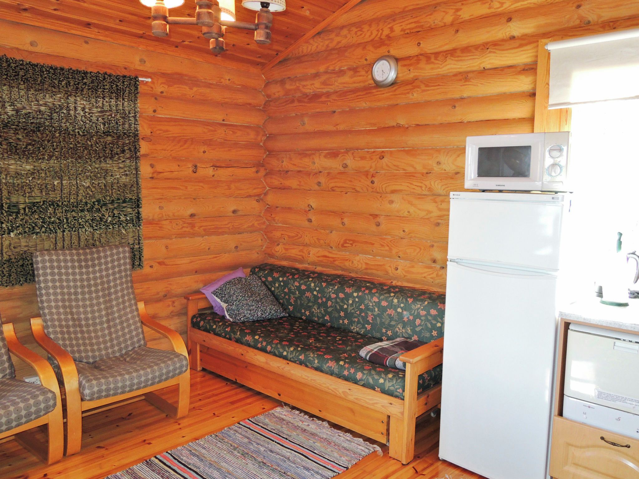 Interior d'una cabana de fusta amb sòl de fusta, un sofà, una cadira, microones i nevera.