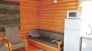 Interior d'una cabana de fusta amb sòl de fusta, un sofà, una cadira, microones i nevera.