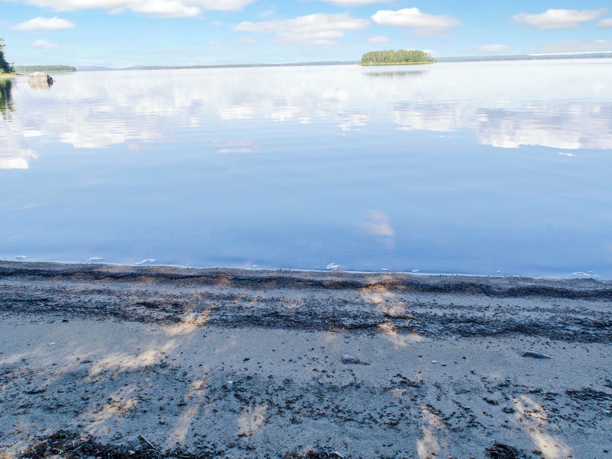 A calm lake with a sandy beach and a small island in the distance.