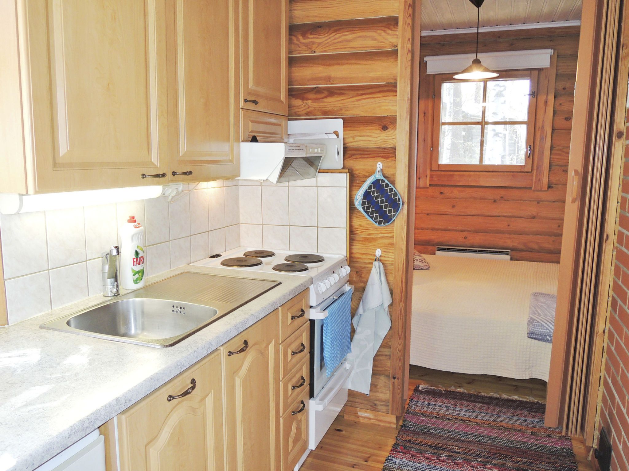 Een kleine keuken met houten kastjes, een spoelbak, een fornuis en een raam.